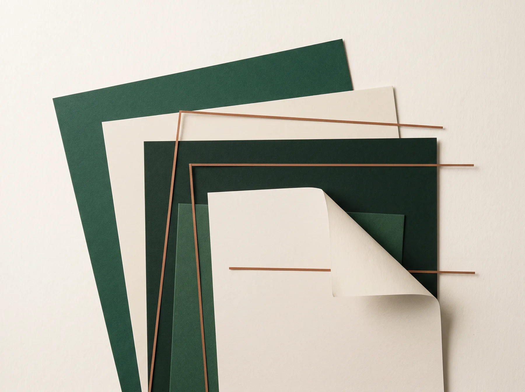 Overhead arrangement of layered cream and pine-green paper sheets with fine copper rules